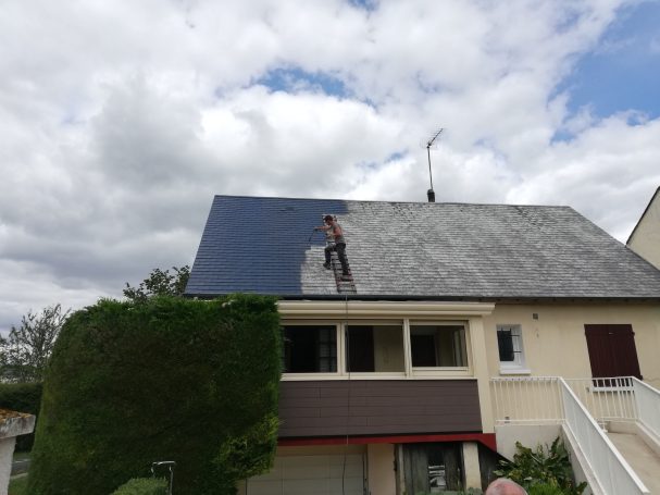 Ouvrier nettoyant des panneaux solaires sur un toit sous un ciel nuageux.