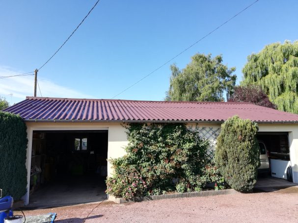 Maison avec un toit en tuiles, entourée de verdure et d'un ciel bleu.
