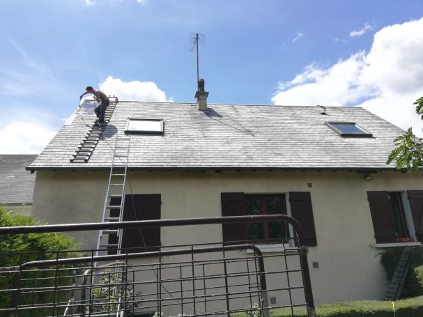 Un homme répare le toit d'une maison sous un ciel ensoleillé.